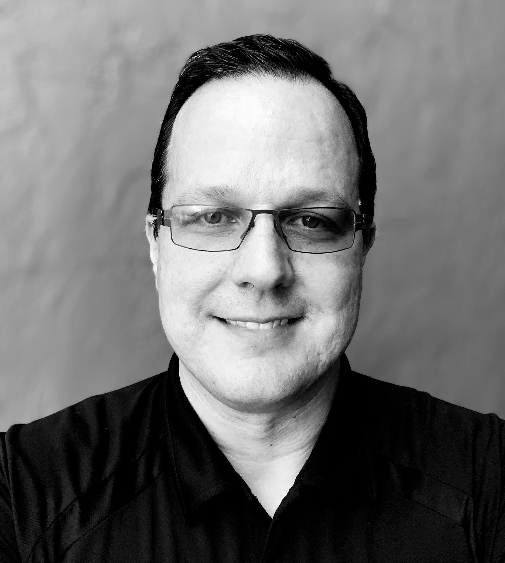 Person wearing a dark shirt against a plain background.